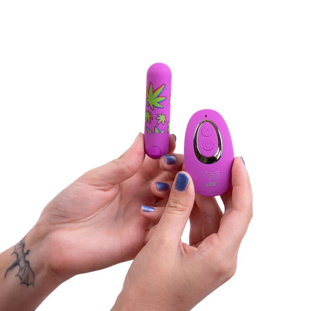 Maia Jessi 420 leaf-print bullet balanced on a fingertip beside the remote