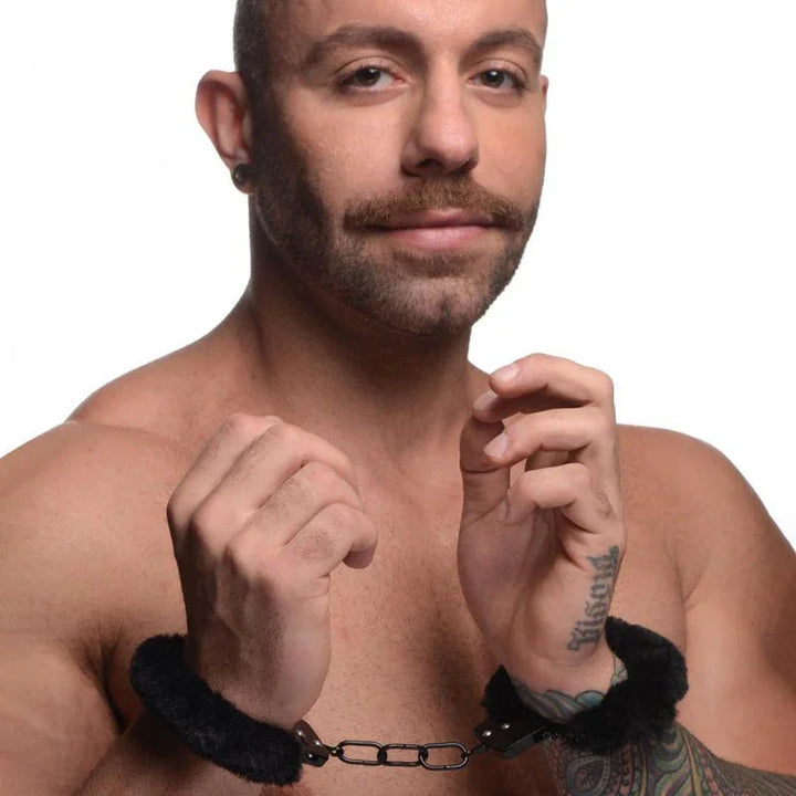 Cuffed in Fur black furry handcuffs worn on a man's wrists, hands raised