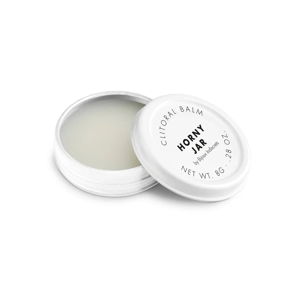 A round, white container with a screw-on lid reveals a solid balm. The lid reads Clitherapy Balm Horny Jar by Bijoux Indiscrets, with Net Wt. 8g, .28 oz. This clitoral balm enhances your experience with its warming effect.