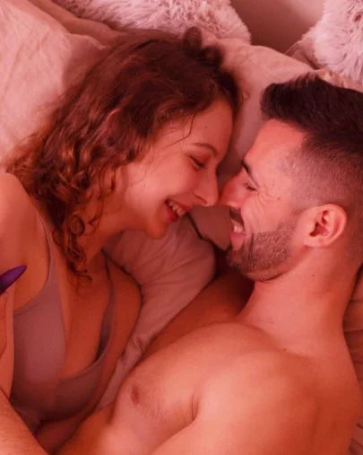 A laughing couple nose to nose, tangled in soft white bedding