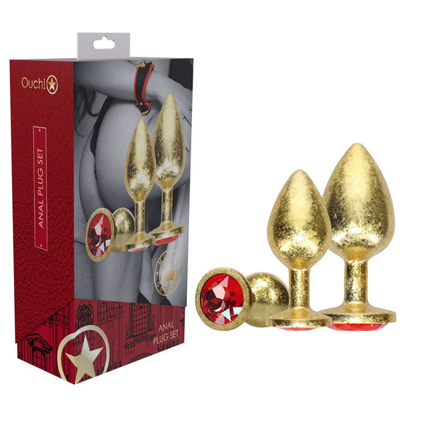OUCH! Milan Metal Anal Plug Set of 3 in Gold, retail box beside three gold plugs with ruby gem bases