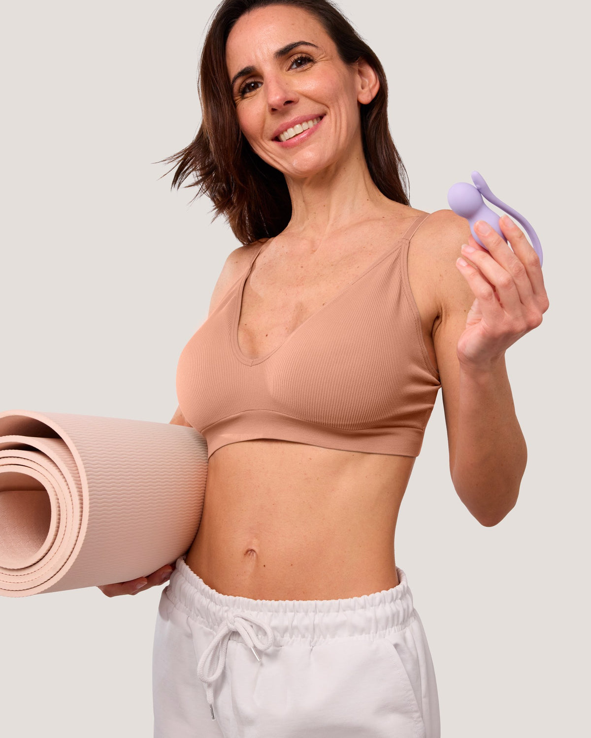 Smiling woman with a rolled yoga mat holding a lilac Perifit Care+