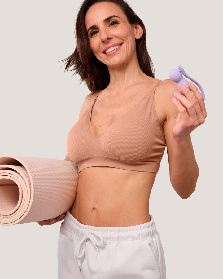 Smiling woman with a rolled yoga mat holding a lilac Perifit Care+