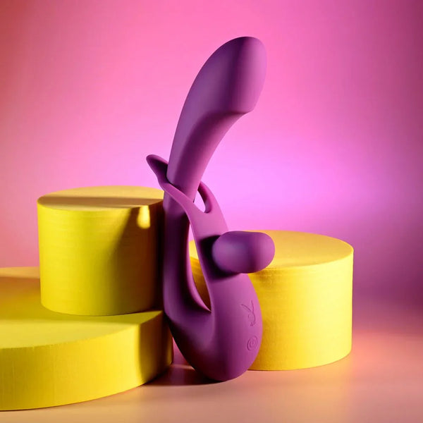 Purple Cha Cha Slide rabbit vibrator propped on yellow podiums under pink light
