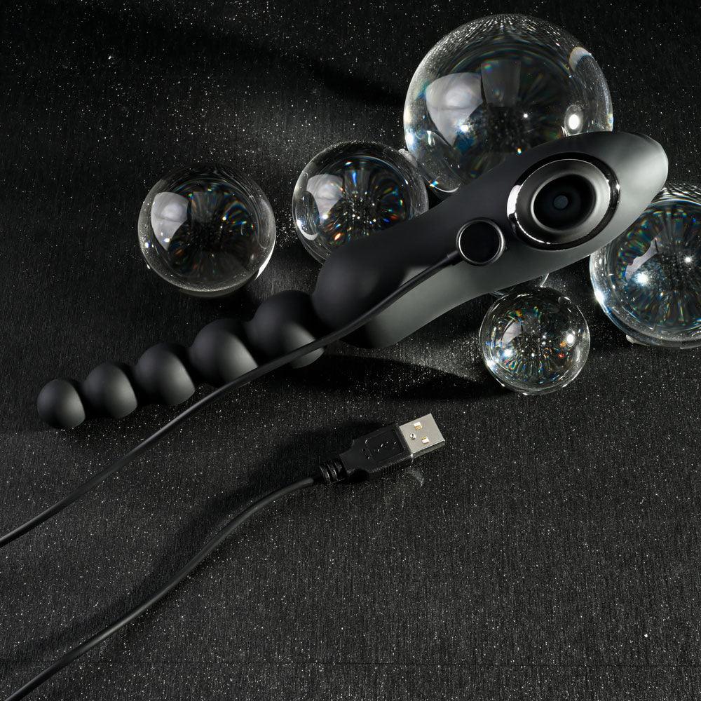 Black Let It Bead lying among glass spheres with its USB charging cable attached