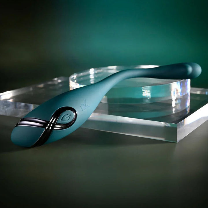 Green Pinpoint Perfection vibrator resting on a clear acrylic block, tail curved