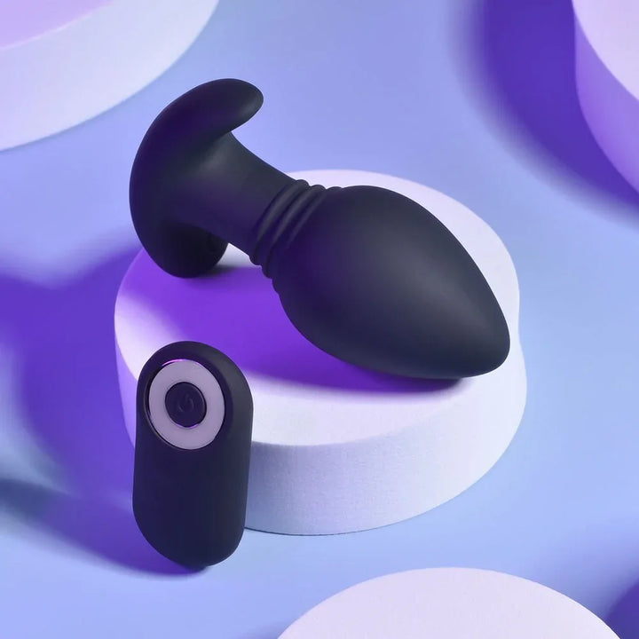 Black Plug & Play butt plug on a white podium with its round wireless remote below