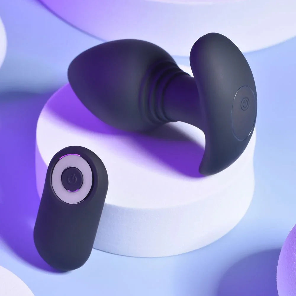 Black Plug & Play butt plug lying on a white plinth beside the remote control