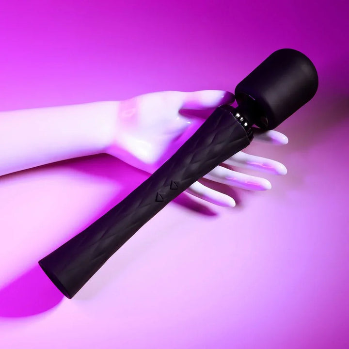 Royal massage wand laid across a white display hand under magenta lighting