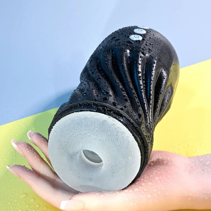 Black Solo stroker held in a wet hand, water droplets on the ribbed casing
