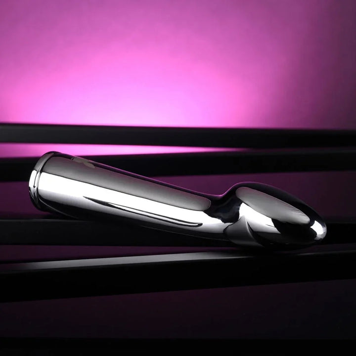 Chrome Swoon vibrator lying on a dark reflective surface, tip to the left