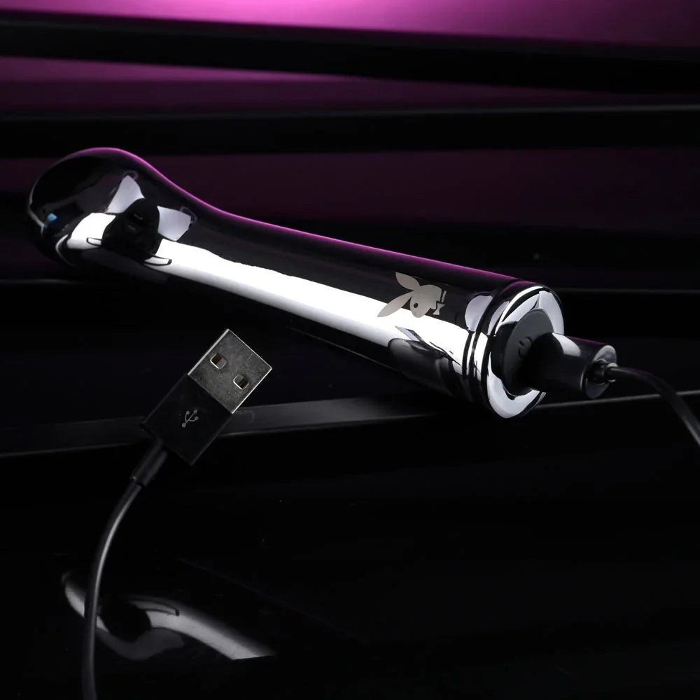 Chrome Swoon vibrator lying down with its USB charging cable plugged in
