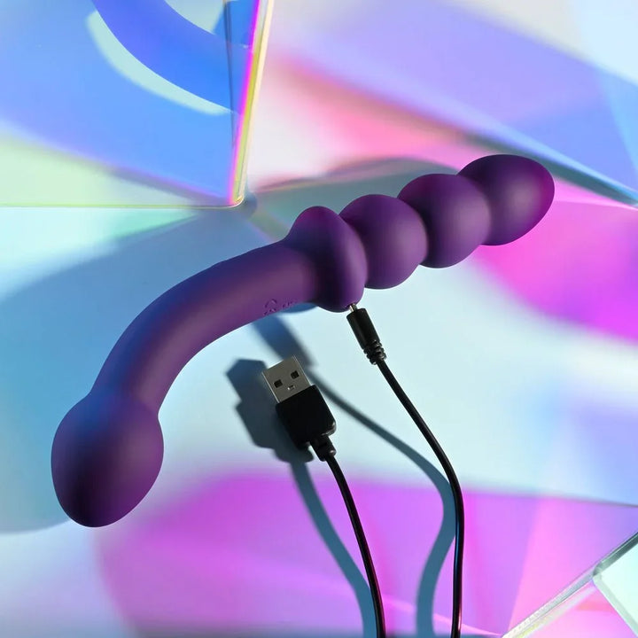 Purple Seeker vibrator with its USB charging cable connected beside the beaded end
