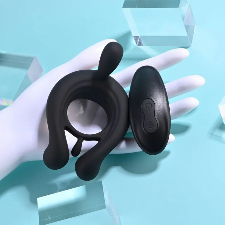Black Triple Play cock ring resting against a white hand with the remote beside it