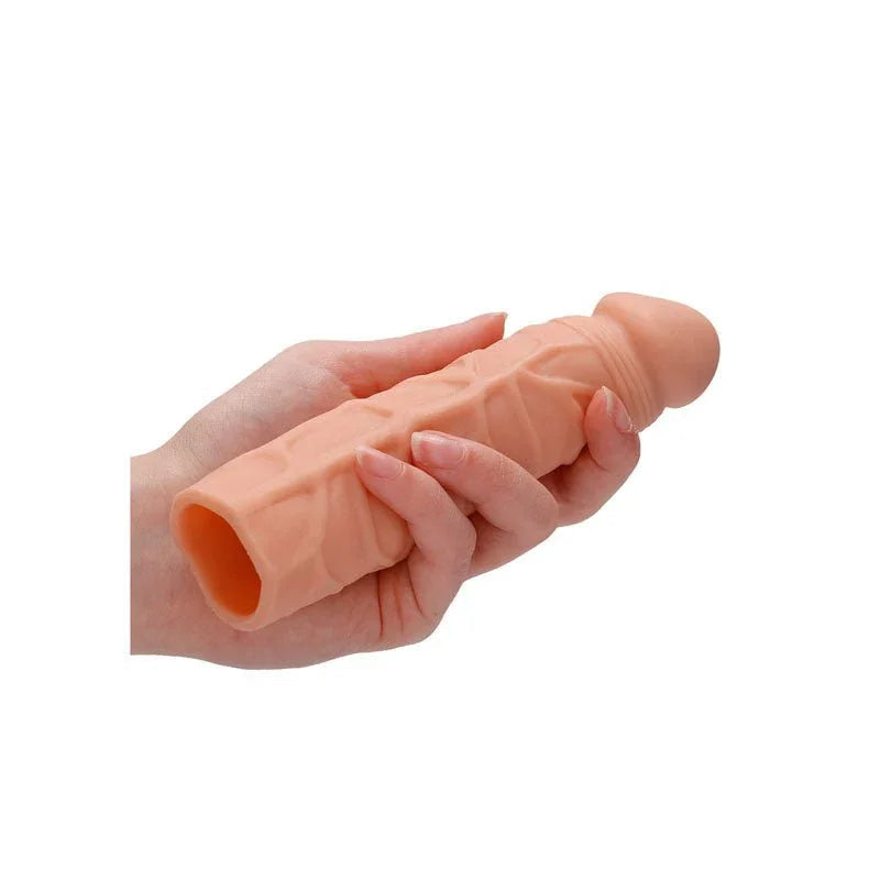 REALROCK 17.8 cm Penis Extender Sleeve in Flesh, held in one hand showing the hollow open end
