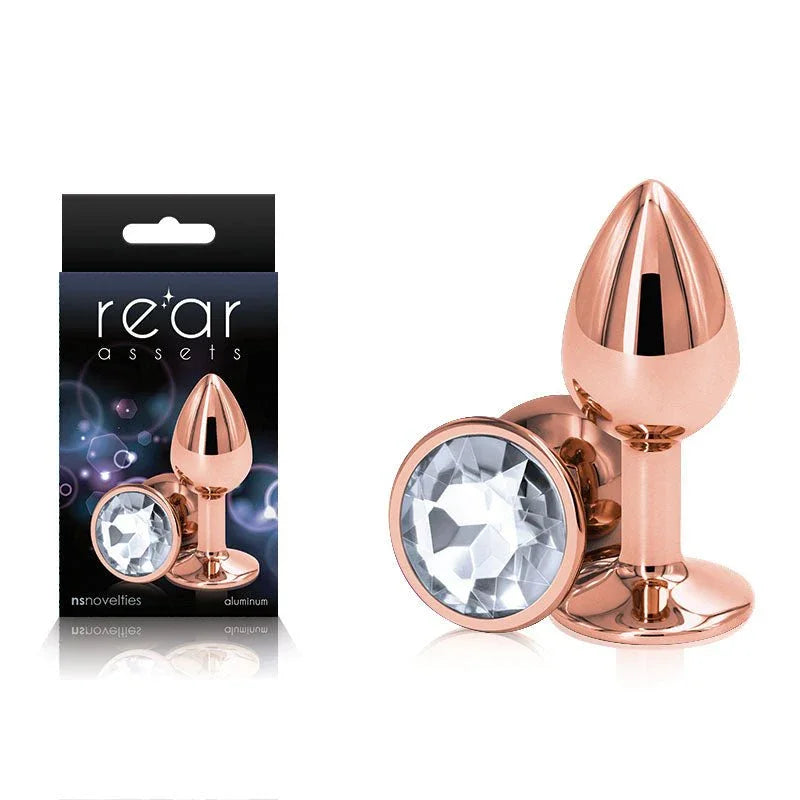 Rear Assets small metal butt plug in Rose Gold with a clear gem base, beside its box