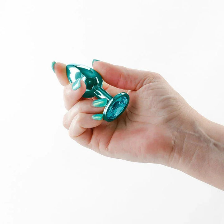 Rear Assets small metal butt plug in Teal held between finger and thumb for scale
