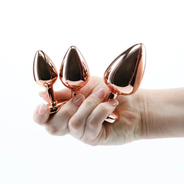 Rear Assets Trainer Kit in Rose Gold, three metal plugs held in a hand for scale