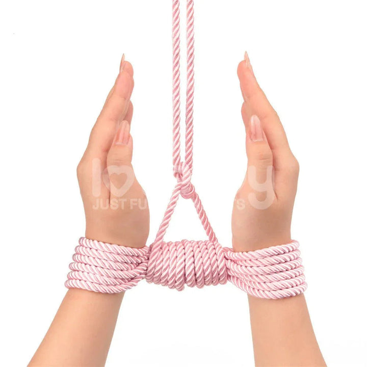 Two wrists tied with pink silky rope and lifted by an overhead line