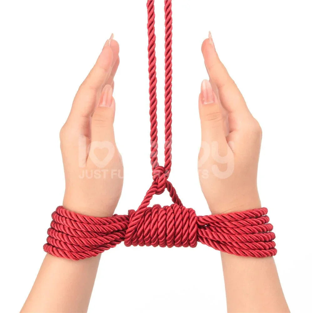 Wrists bound together with red silky rope and drawn up by a suspension line
