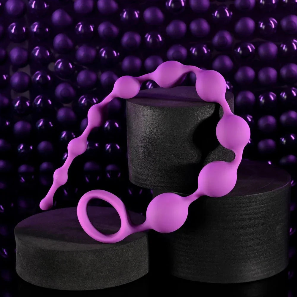 Purple anal beads draped over black plinths against a beaded backdrop