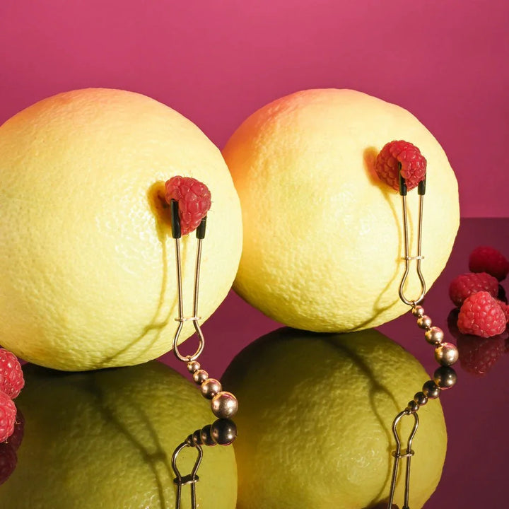 Beaded nipple clamps gripping raspberries set on two lemons