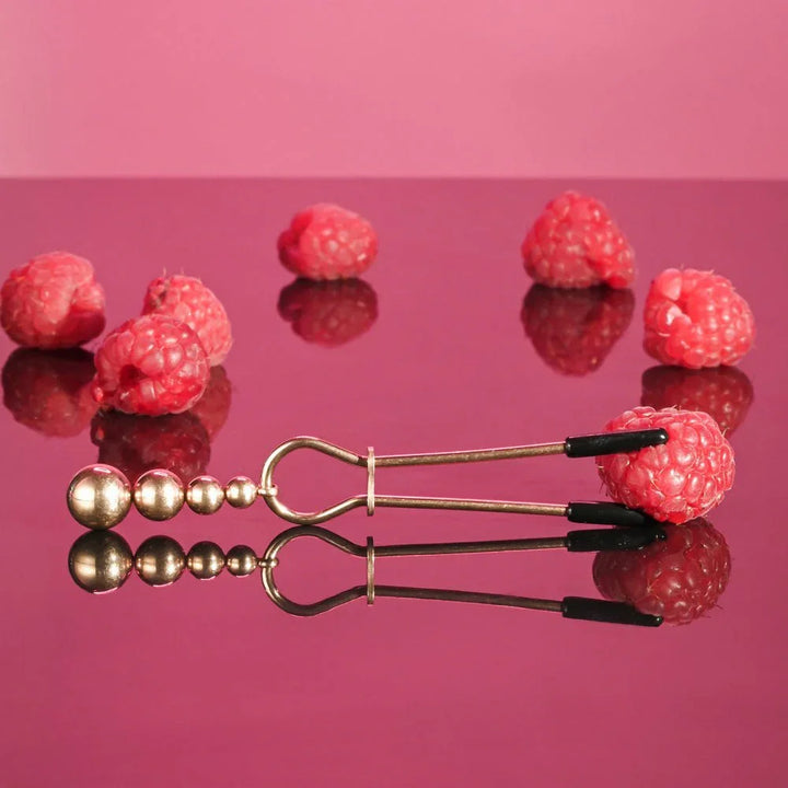 Two rose gold beaded clamps upright, one gripping a raspberry