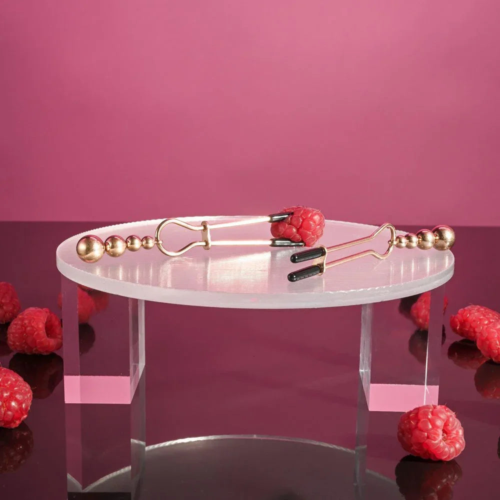 Beaded nipple clamps on the edge of a clear riser with the bead tails hanging