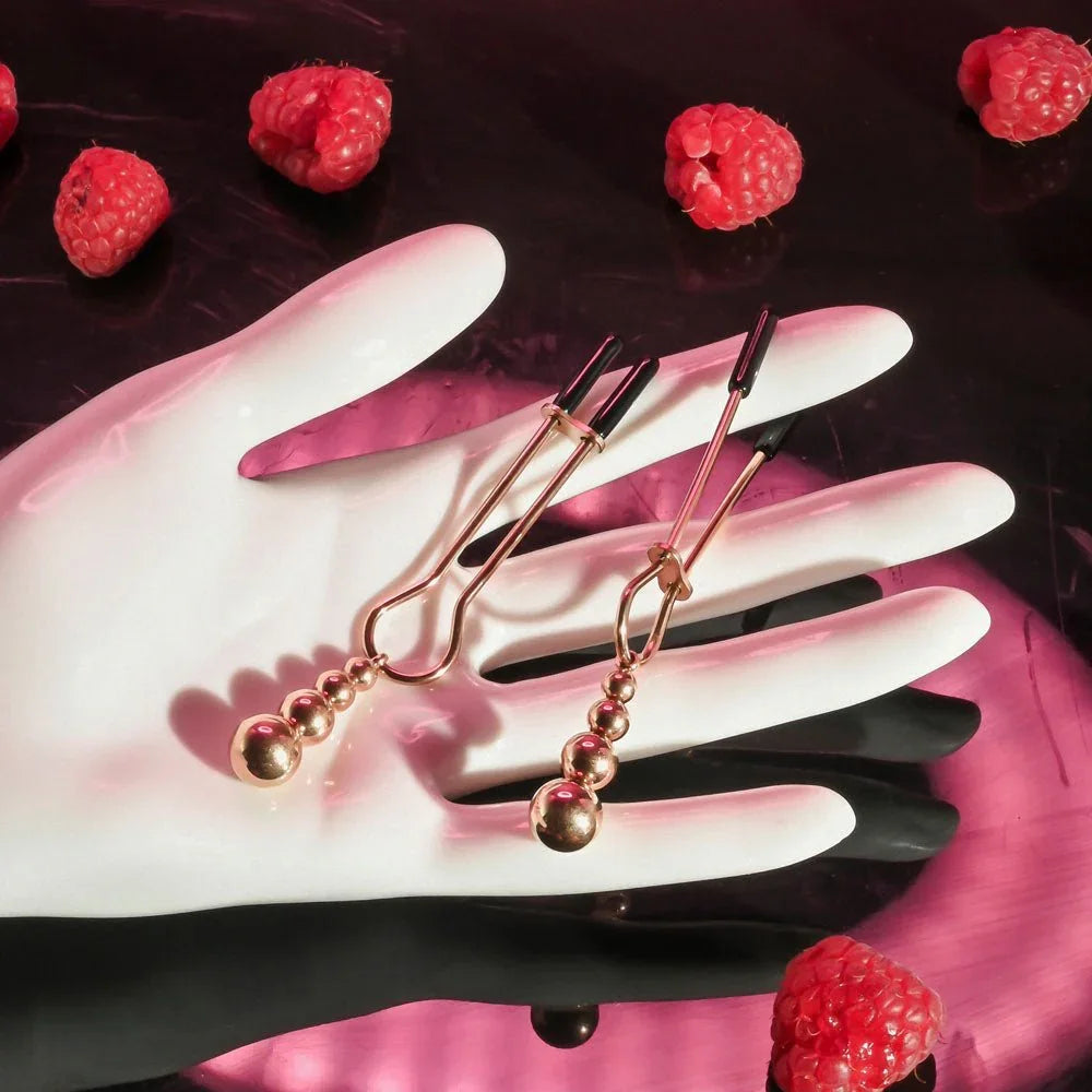 Rose gold beaded nipple clamps laid across a white mannequin hand