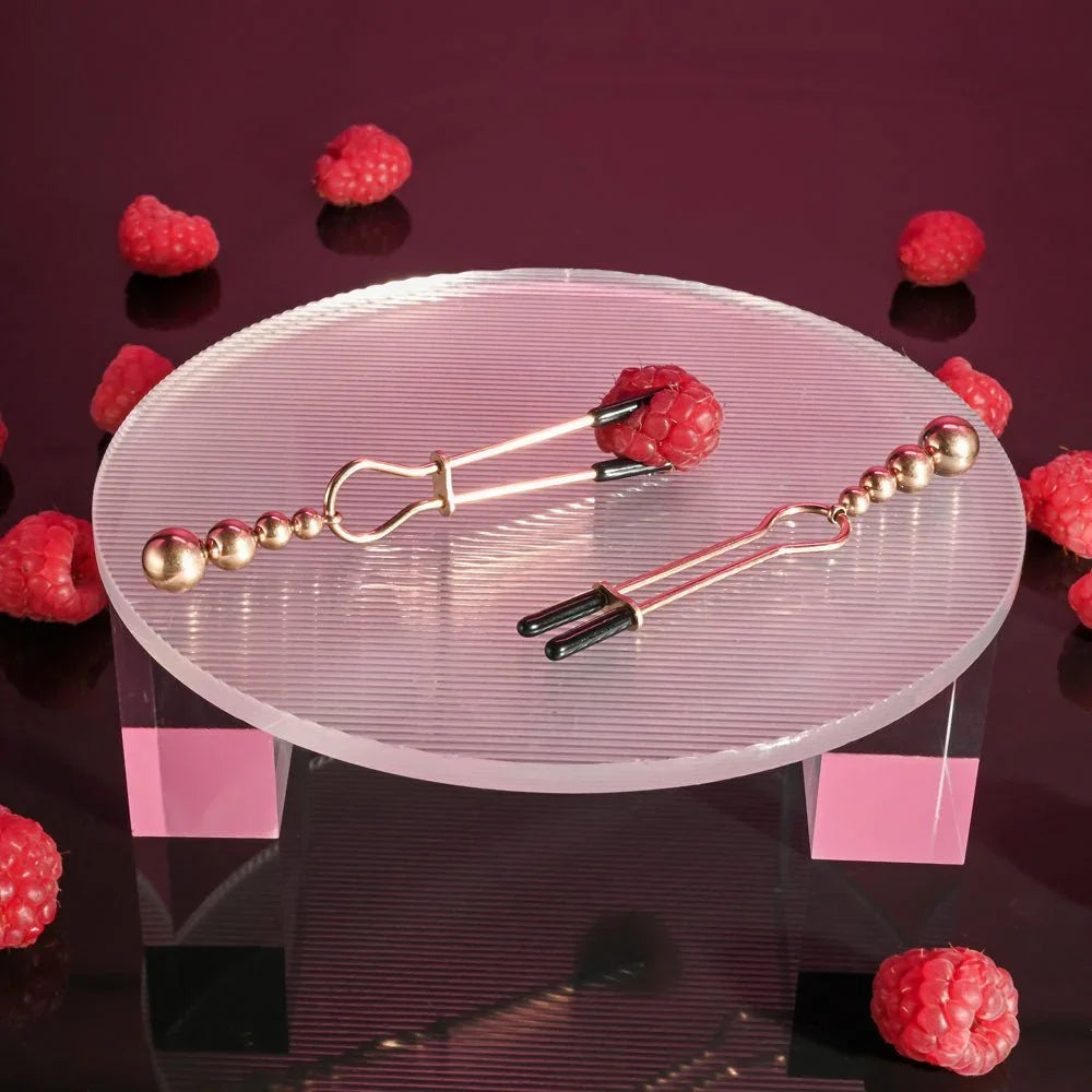 Rose gold beaded clamps laid on a clear riser surrounded by raspberries