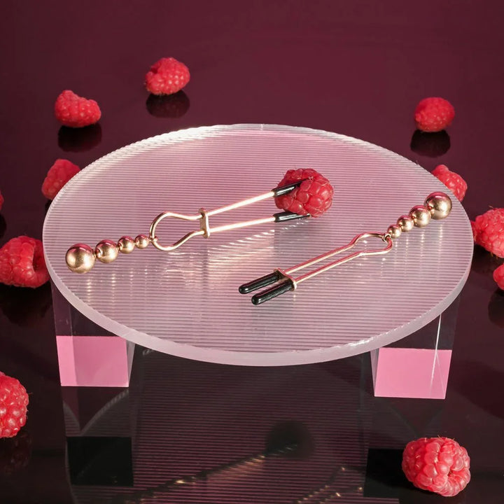 Rose gold beaded clamps laid on a clear riser surrounded by raspberries
