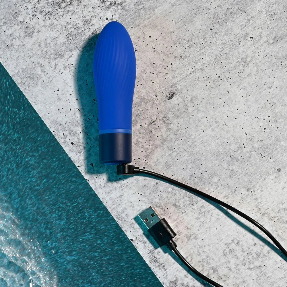 Cobalt Cutie bullet with its charging cable attached at the base, on grey concrete