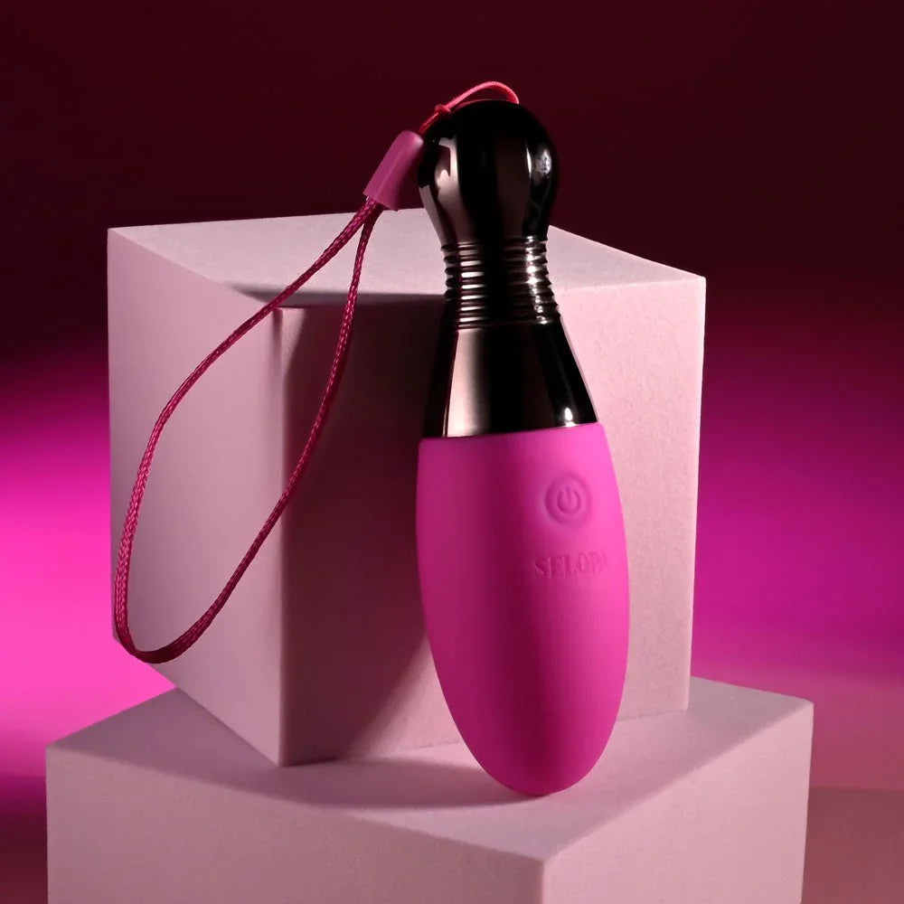 Companion egg leaning against a pink plinth with the wrist cord looped beside it