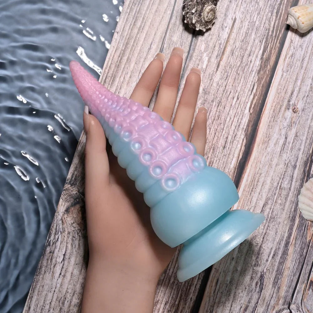 Stuck On You tentacle dildo held on a hand against driftwood