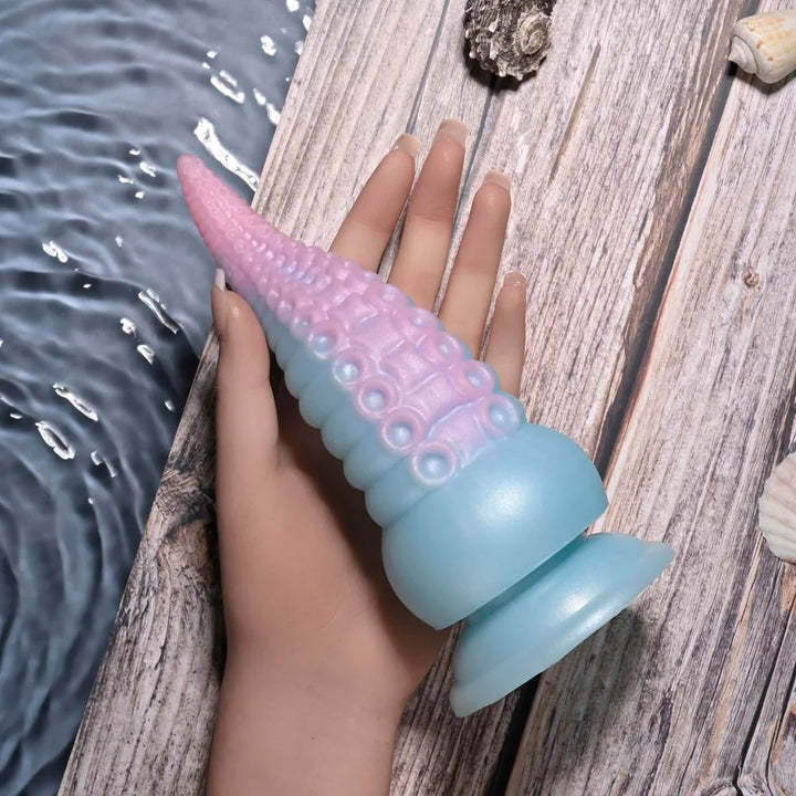 Stuck On You tentacle dildo held on a hand against driftwood
