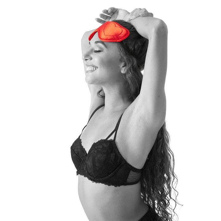 Model with arms raised, sliding the red Amor Blindfold onto her head