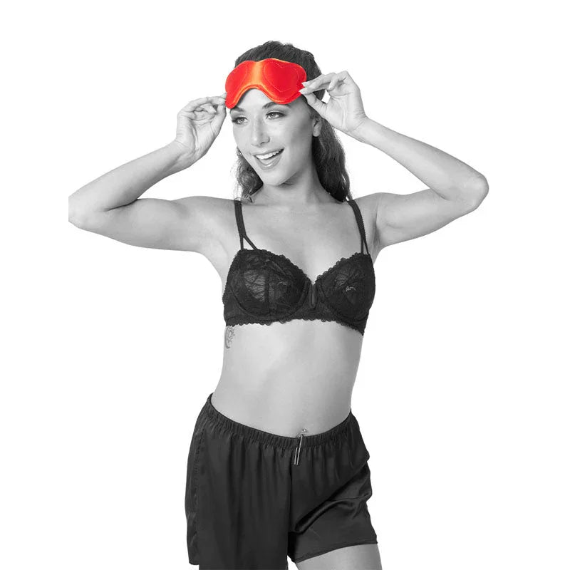 Model standing with both hands on the red heart blindfold at her brow