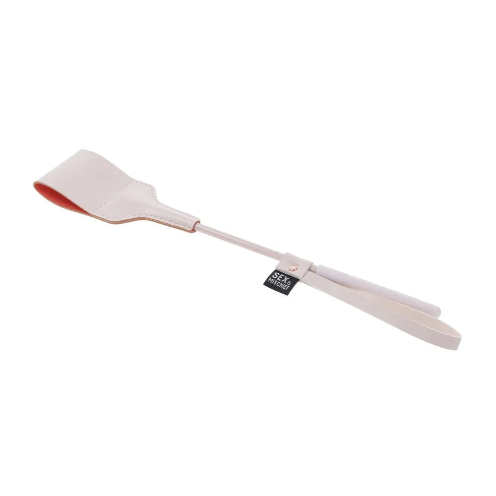 Peach riding crop angled with the flat tip upper left and the shaft trailing
