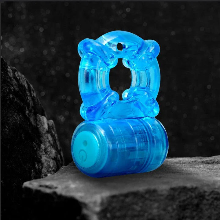 Blue rechargeable cock ring standing on a stone ledge, power button lit on the motor