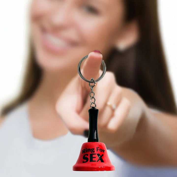 Ring For Sex bell keychain held out on a finger, a smiling woman behind in soft focus